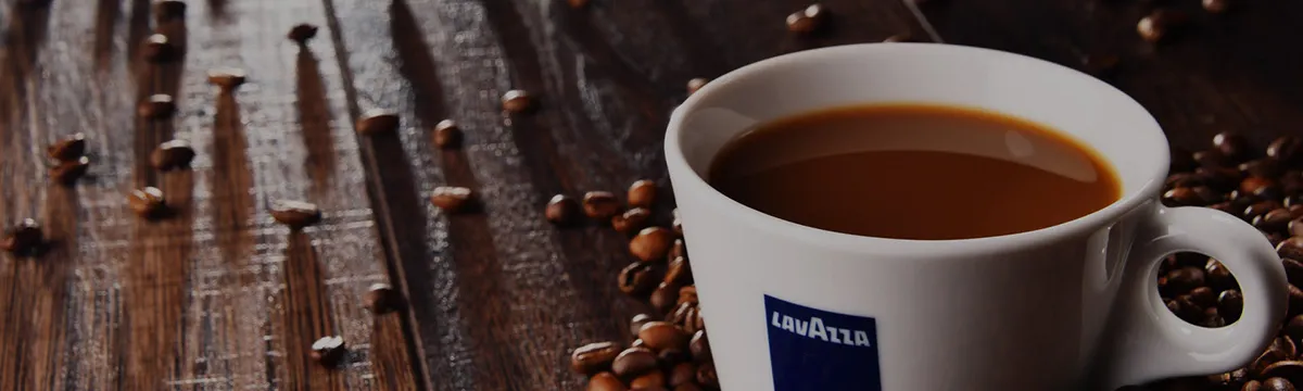 Filiżanka czarnej kawy Lavazza Qualita Oro w otoczeniu ziaren 100% arabica