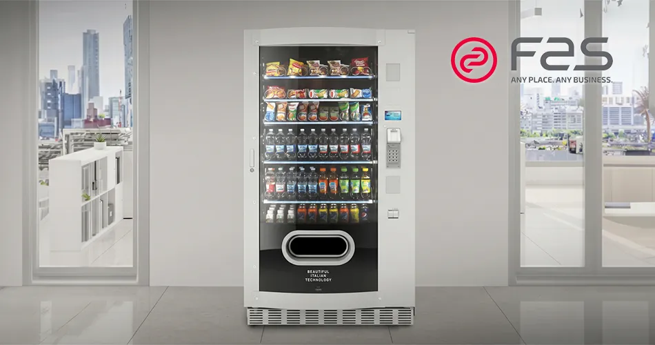 Nowoczesny automat vendingowy FAS do sprzedaży napojów i przekąsek ustawiony w jasnym, przeszklonym wnętrzu biurowym.